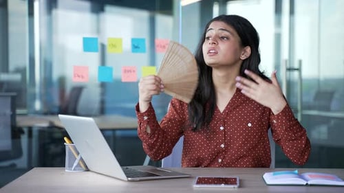 Young businesswoman is hot sitting at the workplace at desk in a modern business office.