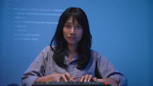 Asiatische Softwareentwicklerin in blauem Hemd, konzentriert sich auf das Tippen von Programmcode