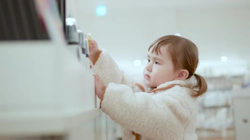 Curious 3 Years Old Girl Picking A Gold Bar Item Displayed Inside A Shopping Mall. - Medium Closeup