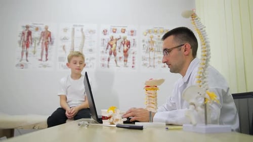 Ein Arzt sitzt an einem Schreibtisch und ein Kind sitzt vor einem Computer