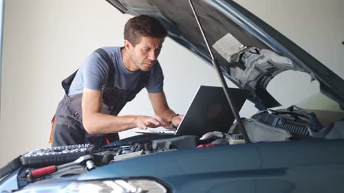 Auto mechanic using laptop for vehicle diagnostics in garage