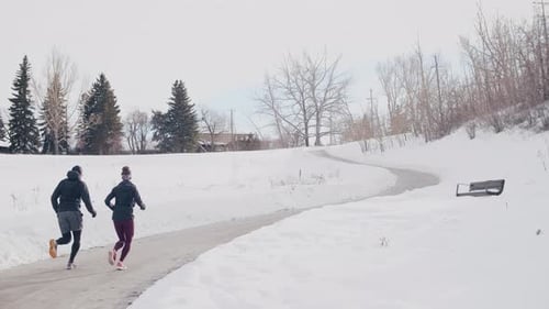 Active couple running on snowy road in Canada during winter exercise