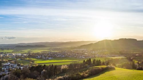 Sunset Illuminates a Town in a Hilly Valley with Forests and Meadows