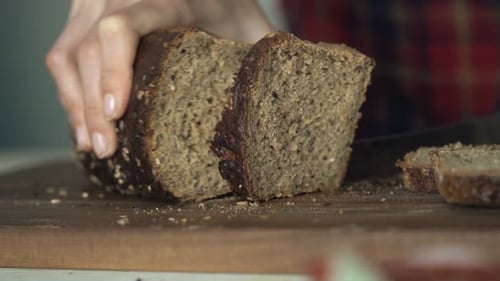 Hands Slice Dark Bread on Wooden Cutting Board