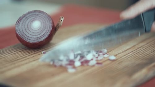 A close up shot of a man cutting onion to slices on a wooden board, shiny silver knife, 4K video