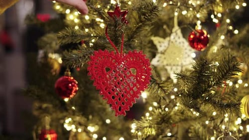 Person Hangs Handmade Red Knitted Heart on Branch of Christmas Tree Closeup