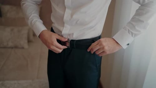 Man Fastens Leather Belt Before Wedding in Bedroom