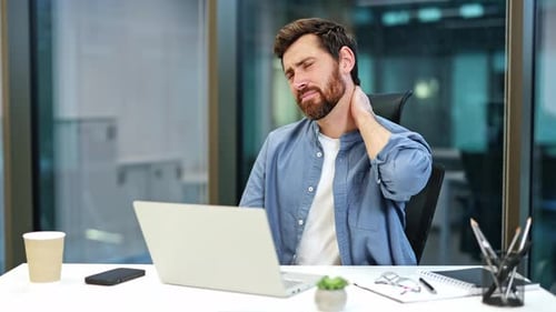 Tired Businessman with Neck Pain Working Late in a Modern Office