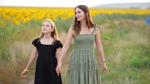 Woman and Teenager Girl Walk Together Past Sunflower Field