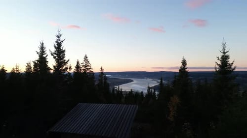 Drone flying trought forest and over shelter revealing town and river right before sunrise