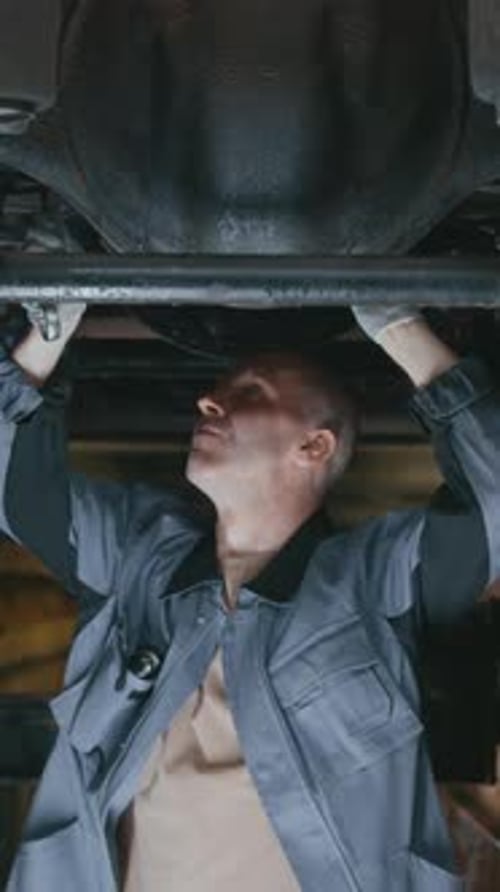 Vertical of Skilled Mechanic Repairing Vehicle on Lift