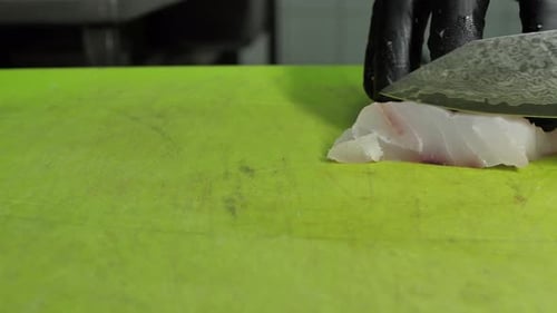 Unrecognizable chef cutting raw fish meat with Damascus steel knife, close up