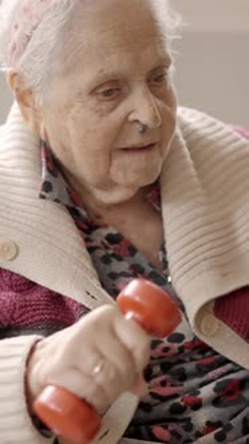 Old Woman Exercising with Dumbbells Sitting on a Nursing Home