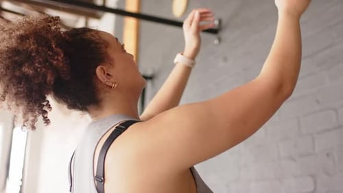Reaching down, woman is gripping and thrusting purple medicine ball against brick wall for strength