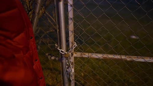 Woman in Red Jacket Holding Key Tries to Unlock a Locked Chain Fence Gate