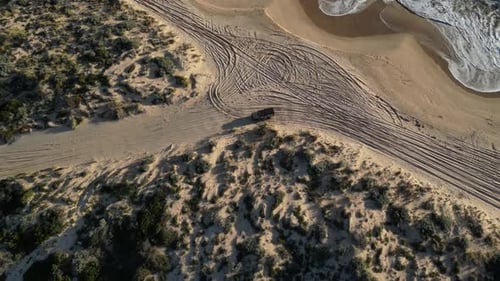 Vehicle leaving beach and driving along unpaved road between sandy dunes, Australia. Aerial top-down