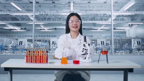 Asian Woman Scientist Looks Through Microscope In A Lab, Smiling And Crossing Arms