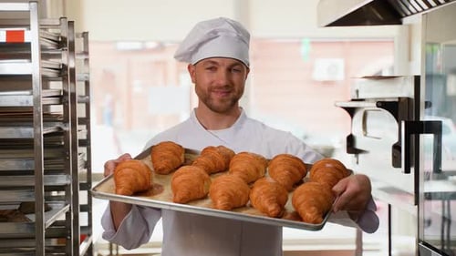 Cheerful Baker Holding Tray of Croissants in Kitchen