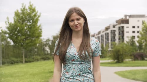 A Beautiful Young Caucasian Woman Waves at the Camera with a Friendly Smile in an Urban Area