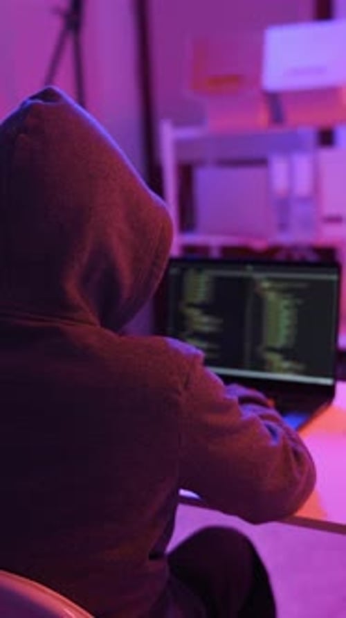Un mystérieux hacker travaillant sur un ordinateur dans une pièce sombre.