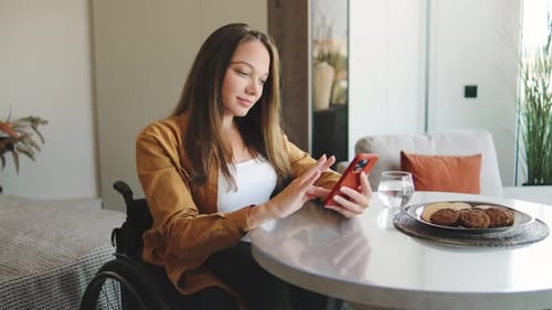 Woman in Wheelchair Using Smartphone at Table