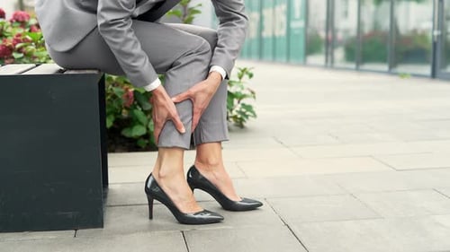 Close up. Female hands massaging leg calf muscle cramps outside. Businesswoman suffers from leg pain