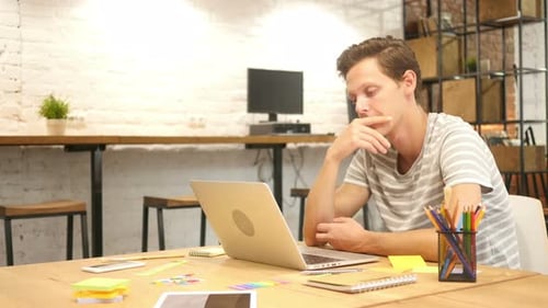Young Man Thinking While Working on Laptop in Office