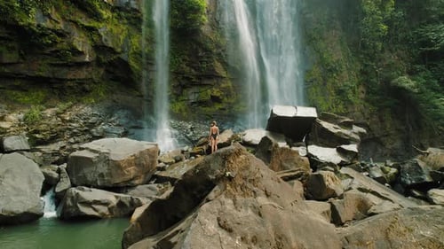 Traveler with outstretched arms stands close to cascading Nauyaca Waterfalls in Costa Rica