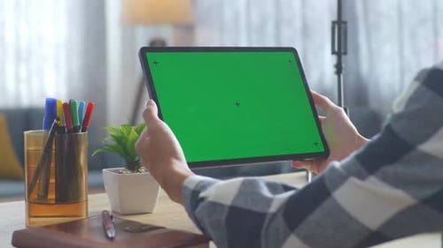 Close up of man's hands holding a mock up green screen tablet on a desk