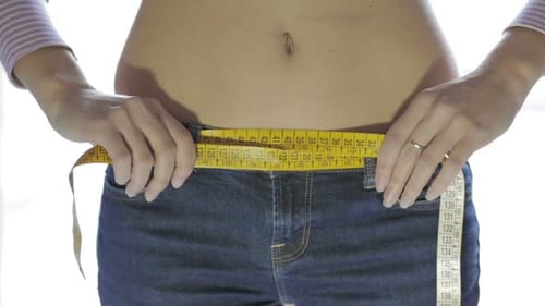 Young Adult Measures Waist with Yellow Tape Measure