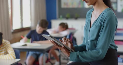 In school, teacher using tablet while students studying in classroom
