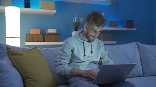 Young Man Using Laptop on Couch at Night