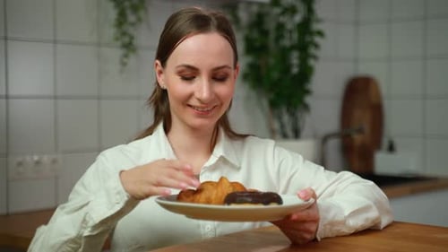Young Adult Eats Croissant and Donut in Kitchen