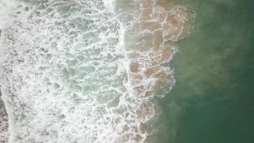 Stormy sea with waves breaking, white foam and beach sand dragged into the sea