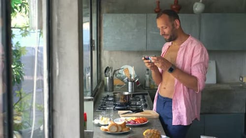 Man uses phone in kitchen while preparing food