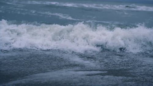 Ocean waves crashing on sandy beach coastline in dark blue powerful storm