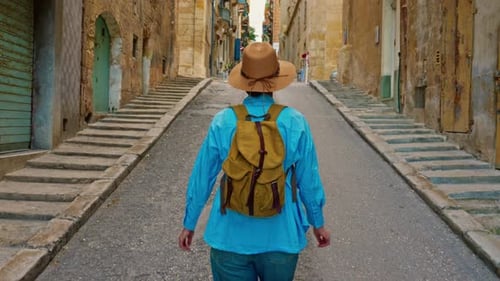 A Female Tourist in a Hat and with a Backpack Walks Along the Traditional Old Streets and Looks at