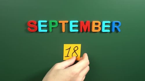 Hand sticking a sticker 18 September calendar day on school board. 18 date of September. Eighteenth