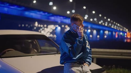 Young Adult Leans on Car Talking on Phone at Night