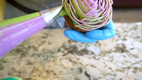 Person Decorating Cupcake With Green and Purple Frosting