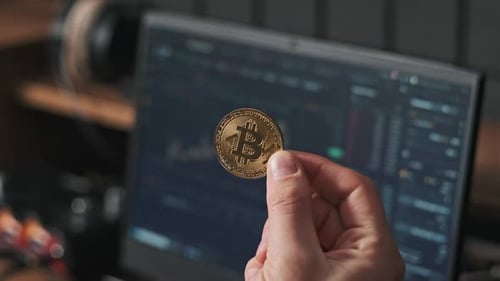 Hand Holding Bitcoin Coin in Front of Laptop