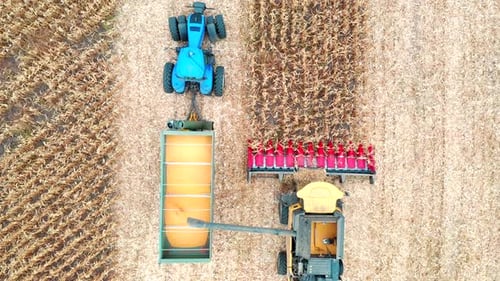 Luftaufnahme eines Mähdreschers, der Maiskörner in einen Traktoranhänger lädt und über die Landwirtschaft fliegt