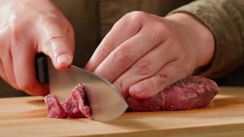Hands Cutting Seasoned Meat on Wooden Board