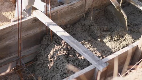 Travailleur pelletant du béton humide dans le coffrage des fondations, des cages à barres d'armature, une consolidation manuelle visible et