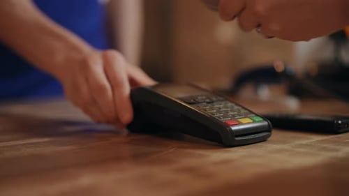 Closeup An Unrecognizable Man in a Blue Apron Pushes a POS Terminal That Stands on a Wooden Counter