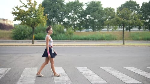 Uma jovem atravessa elegantemente uma rua movimentada em um ambiente urbano durante o dia