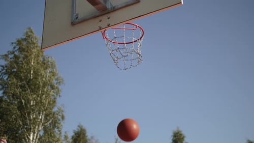 Orangefarbener Basketballball im Korb, nachdem er vom Reifen gegen den blauen Himmel gesprungen ist