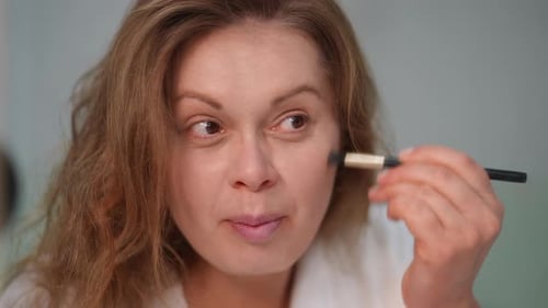 Woman Applies Makeup with Brush in Bathroom