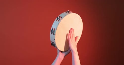 Hands Playing a Tambourine on an Orange Background