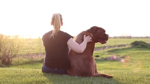 Woman and Dog Sitting Together on Grassy Hill